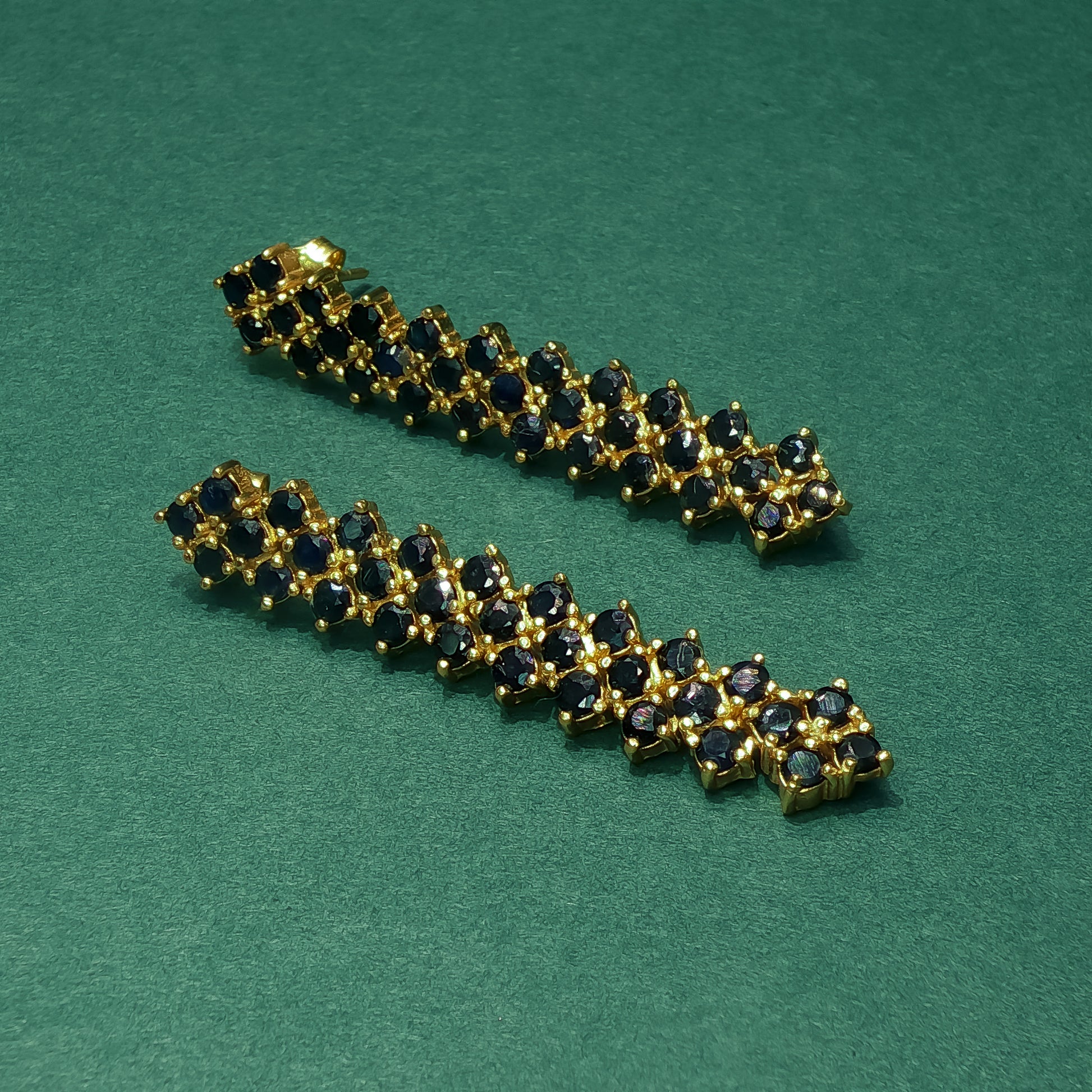 Gold bracelet with black gemstones on a green background

