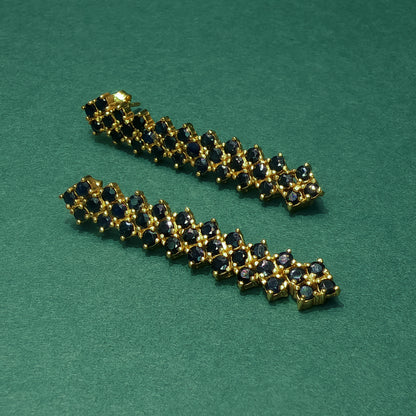 Gold bracelet with black gemstones on a green background

