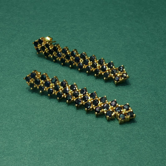 Gold bracelet with black gemstones on a green background

