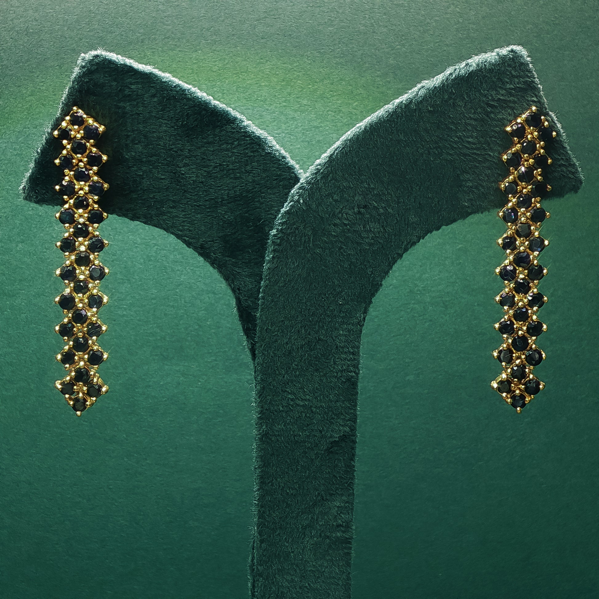 Gold earrings with black stones on a green stand against a green background

