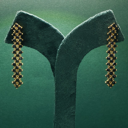 Gold earrings with black stones on a green stand against a green background

