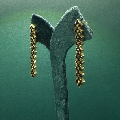Gold earrings on a green stand against a green background

