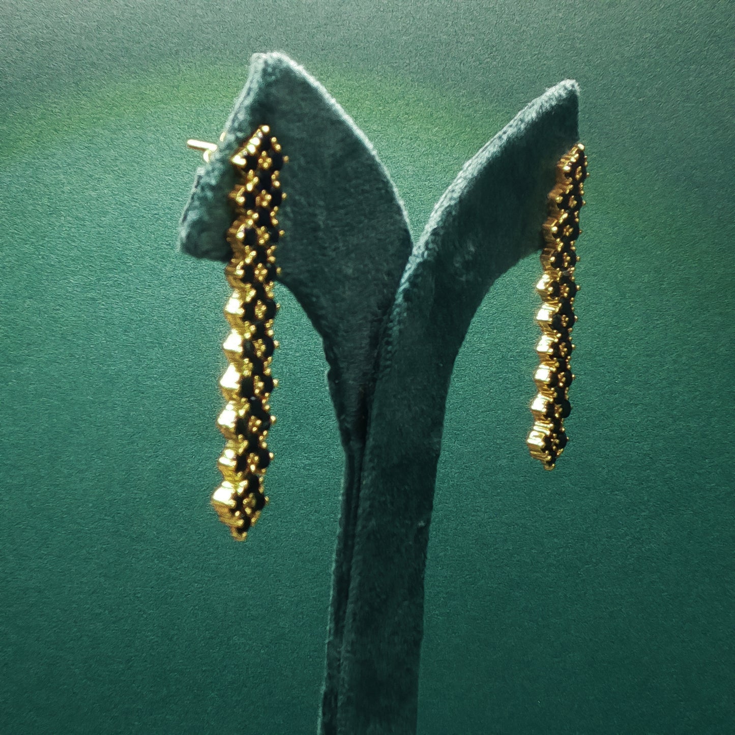 Gold earrings on a green stand against a green background

