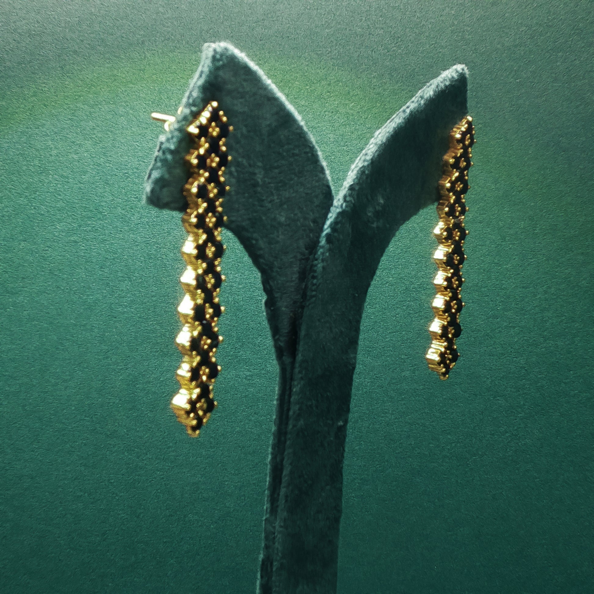 Gold earrings on a green stand against a green background

