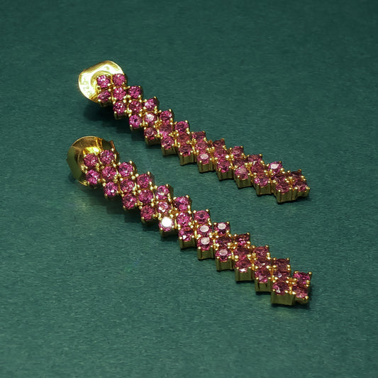 Gold and pink gemstone earring on a green background


