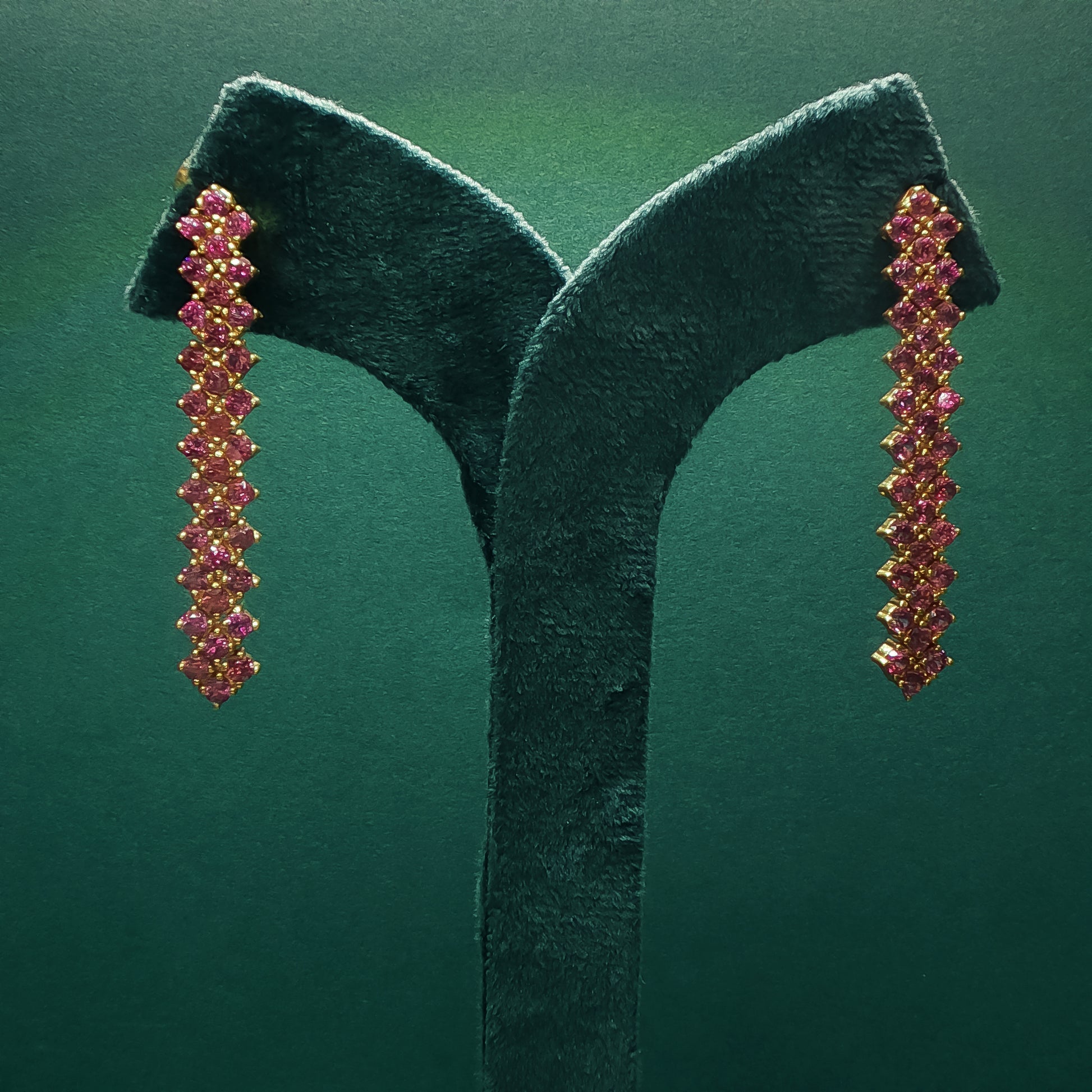 Pair of gold and pink gemstone earrings on a green stand against a green background

