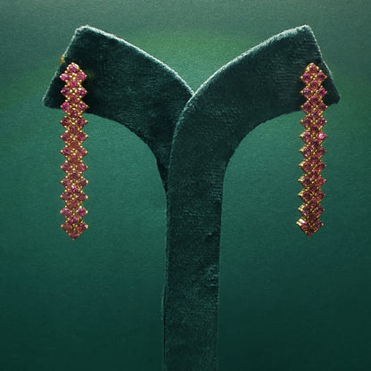 Pair of gold and pink gemstone earrings on a green stand against a green background

