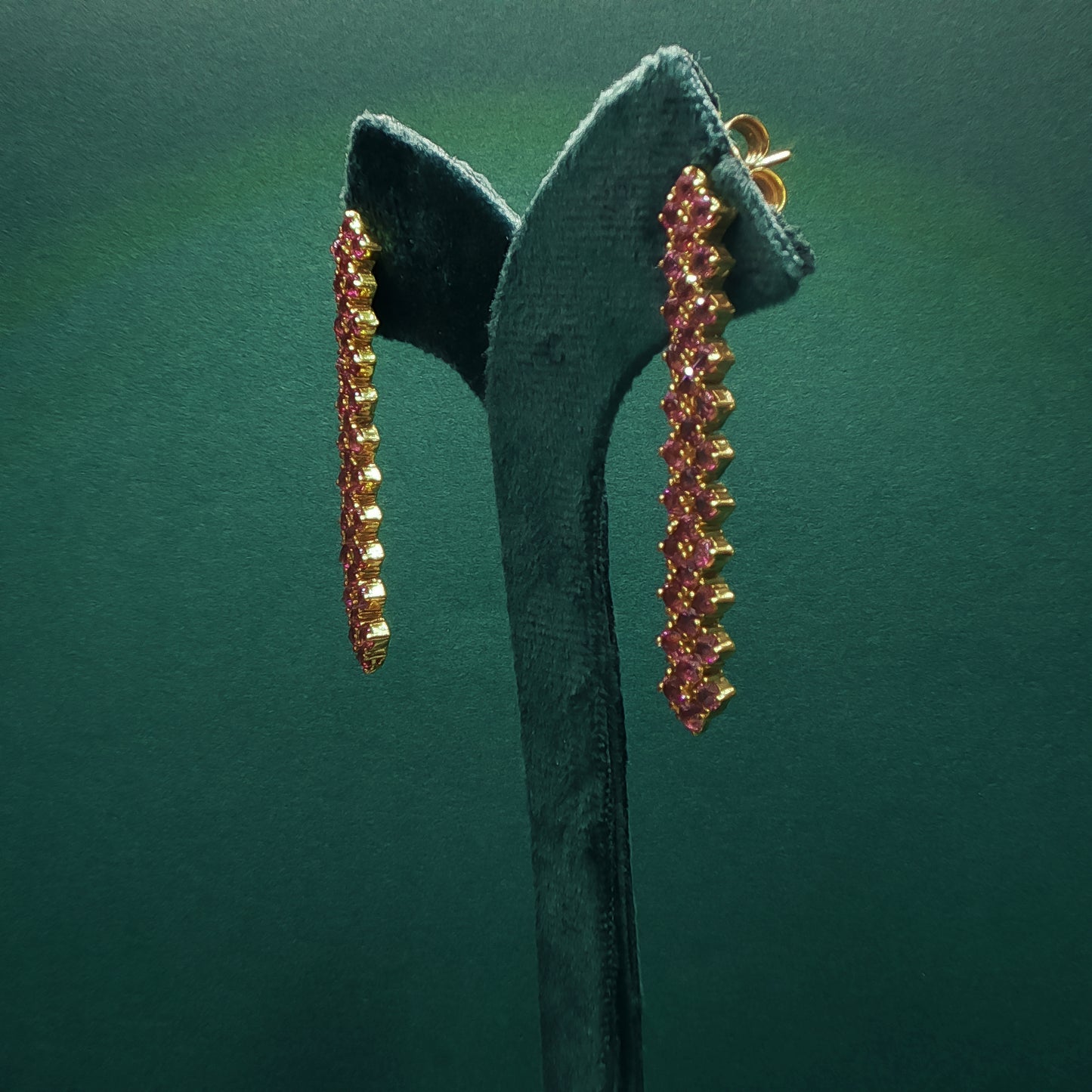 Pair of gold and pink gemstone earrings on a green stand against a green background

