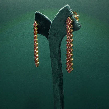 Pair of gold and pink gemstone earrings on a green stand against a green background

