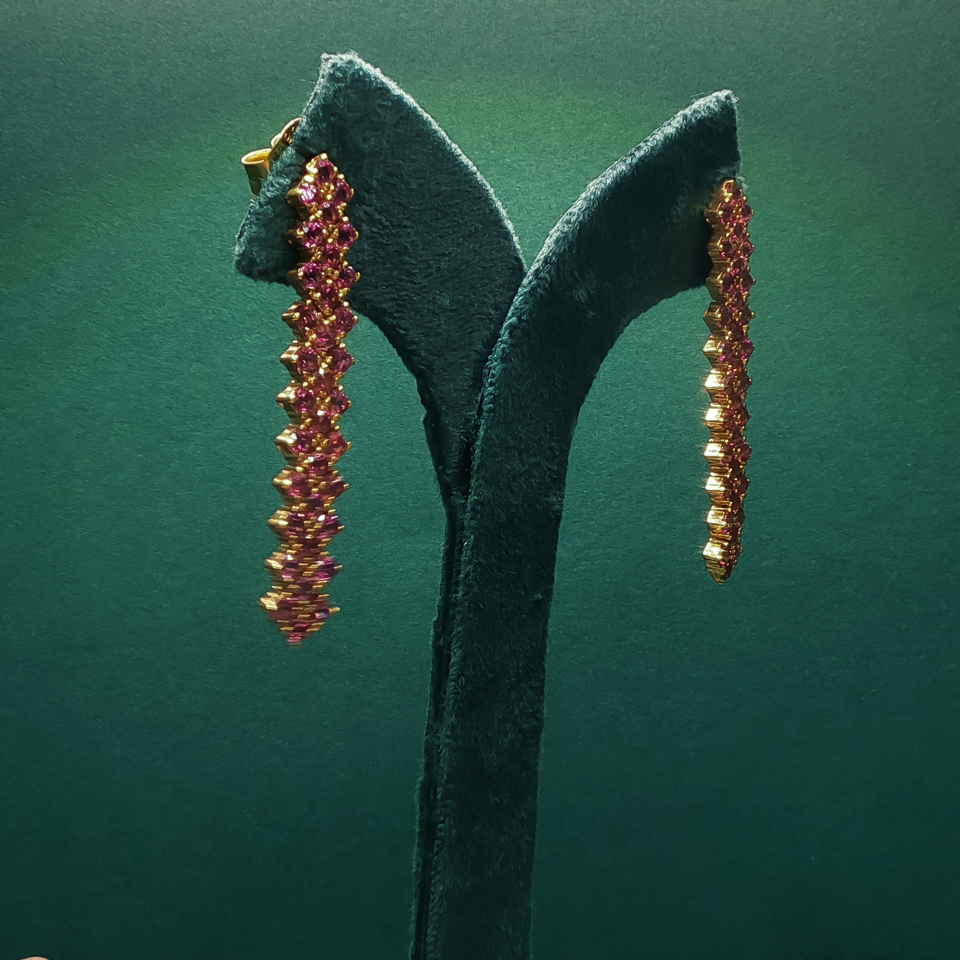 Pair of gold and pink gemstone earrings on a green stand against a green background


