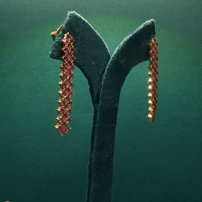 Pair of gold and pink gemstone earrings on a green stand against a green background


