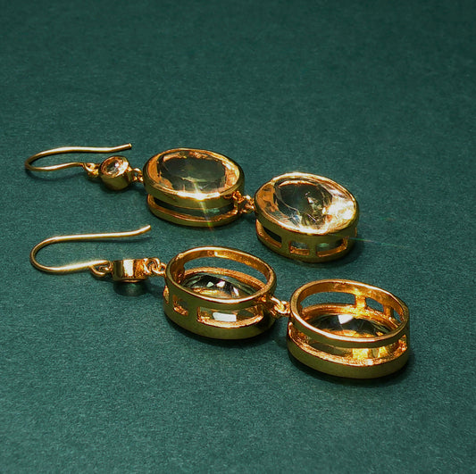 Gold earrings with clear gemstones on a green background

