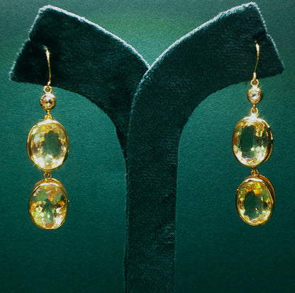 Gold earrings with green gemstones on a green stand against a green background

