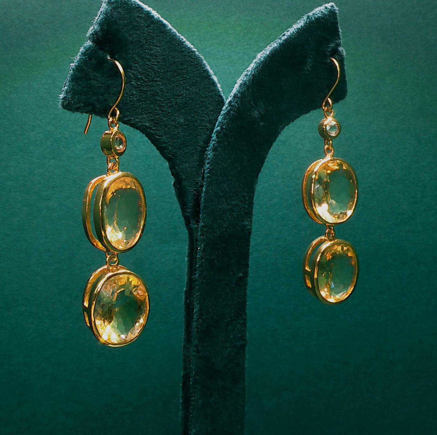 Gold earrings with green gemstones on a green stand against a green background

