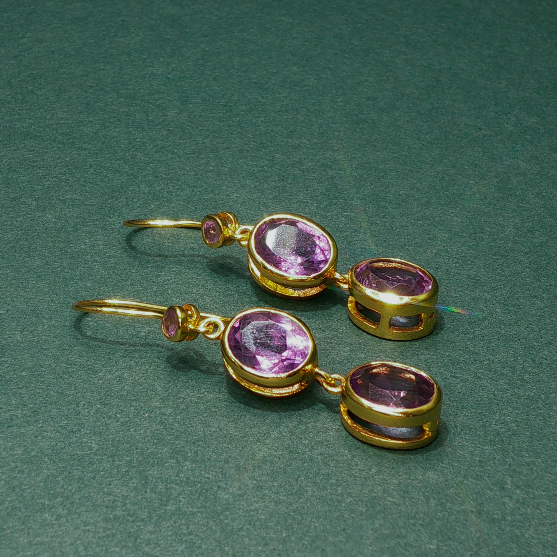 Gold earrings with purple gemstones on a green background

