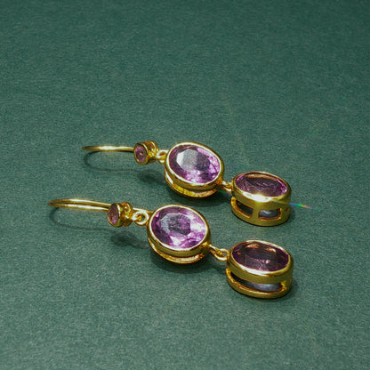 Gold earrings with purple gemstones on a green background

