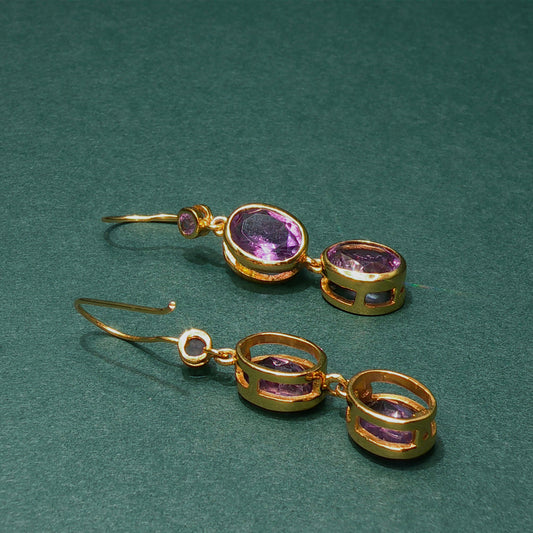 Gold earrings with purple gemstones on a green background

