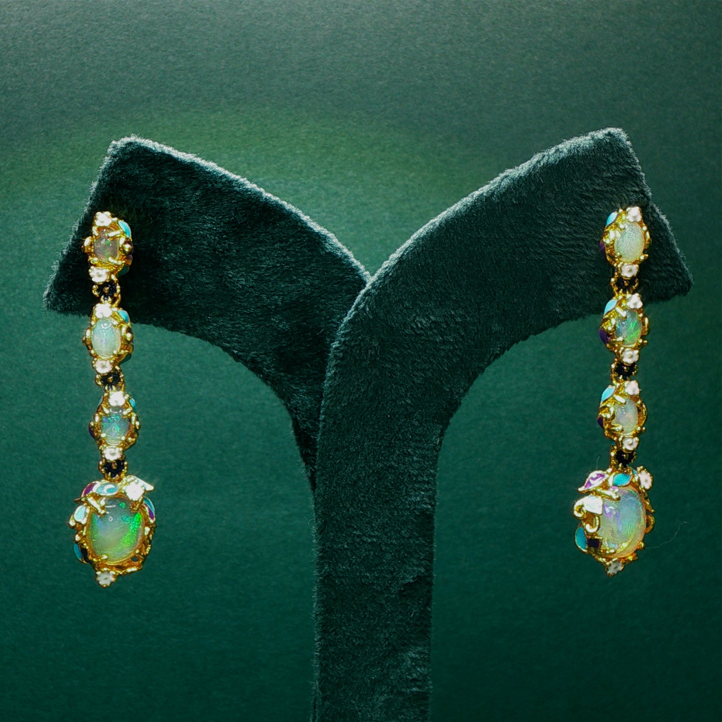 Pair of gold earrings with opal stones on a green stand.