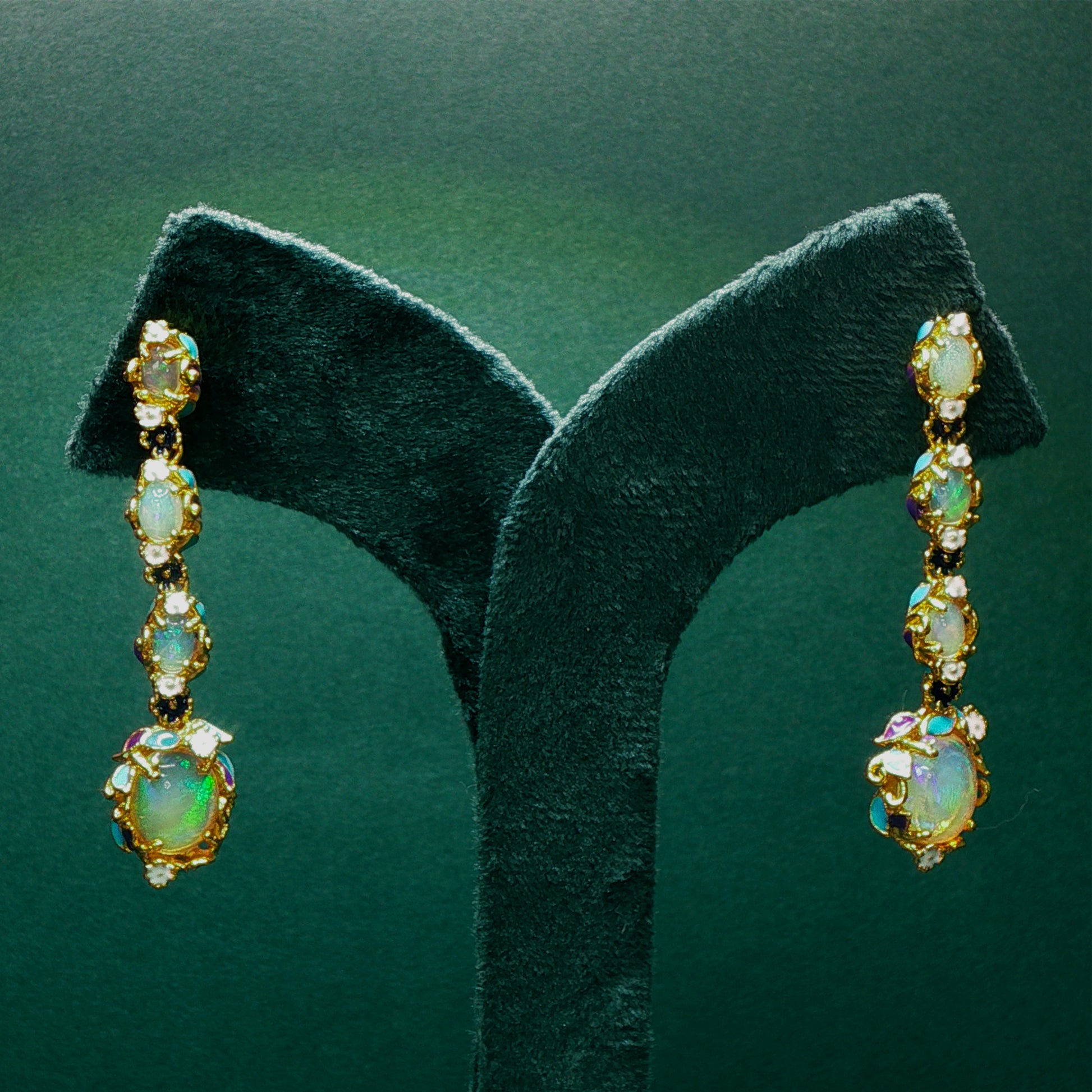 Pair of gold earrings with opal stones on a green stand.