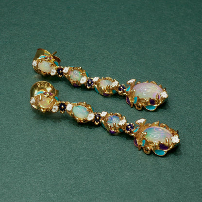 Pair of gold earrings with opal and gemstone accents on a green background


