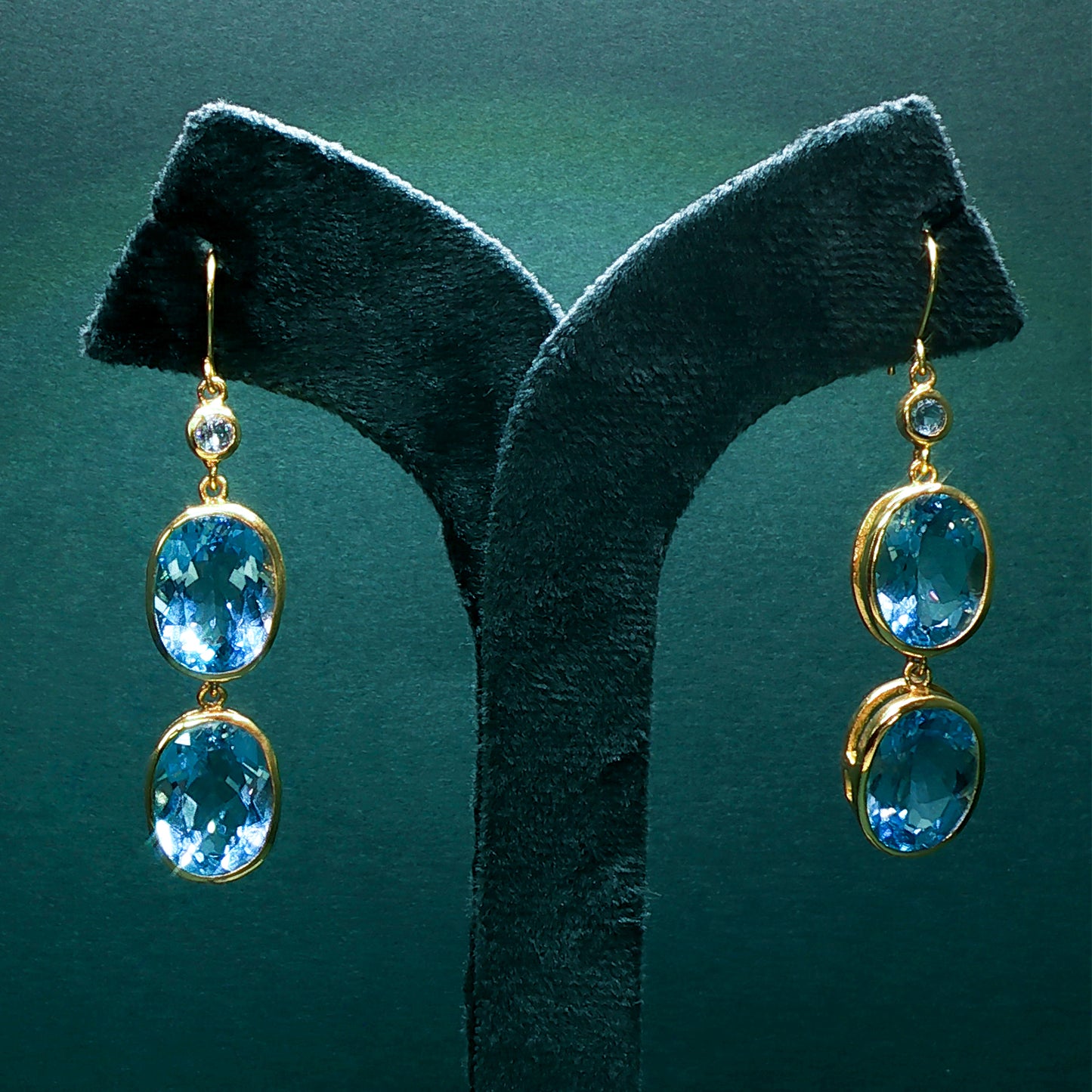 Gold earrings with blue gemstones on a green stand