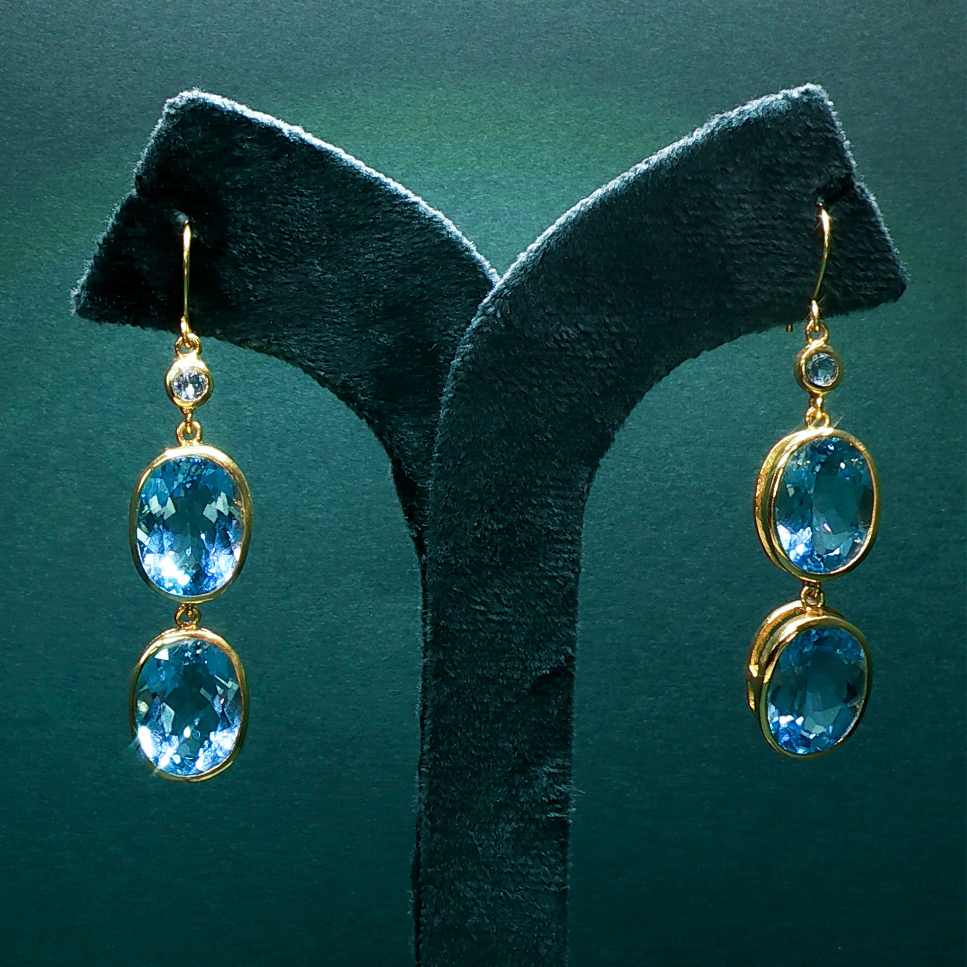 Gold earrings with blue gemstones on a green stand
