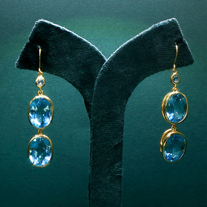Gold earrings with blue gemstones on a green stand
