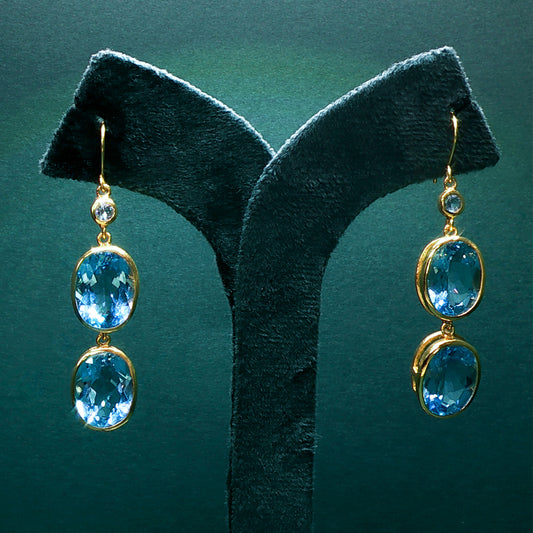 Gold earrings with blue gemstones on a green stand