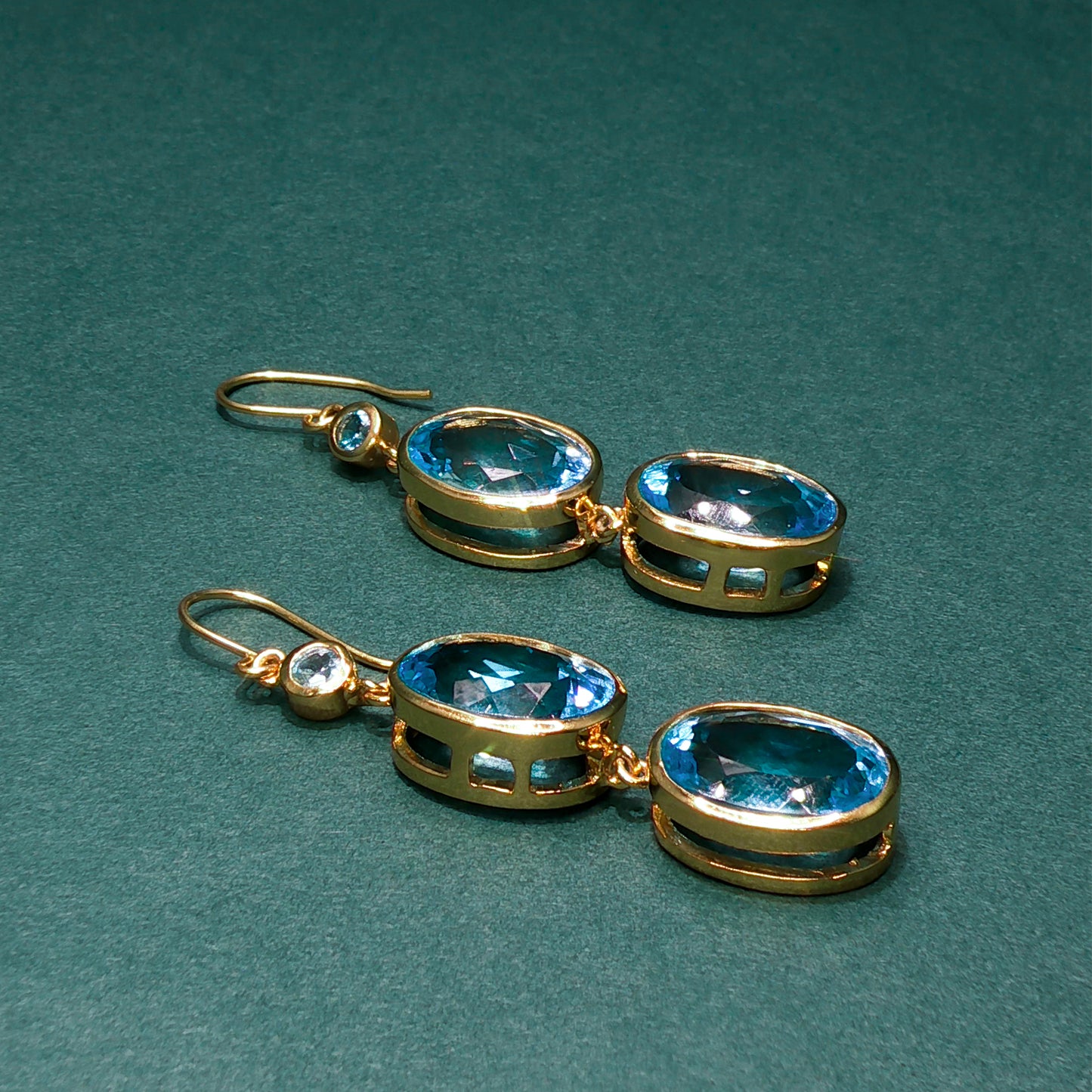Gold earrings with blue gemstones on a green background


