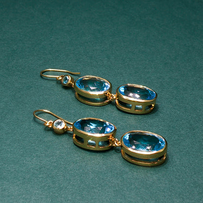 Gold earrings with blue gemstones on a green background

