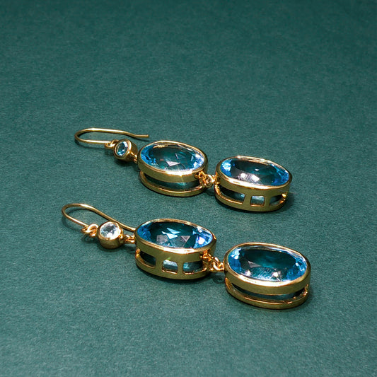 Gold earrings with blue gemstones on a green background

