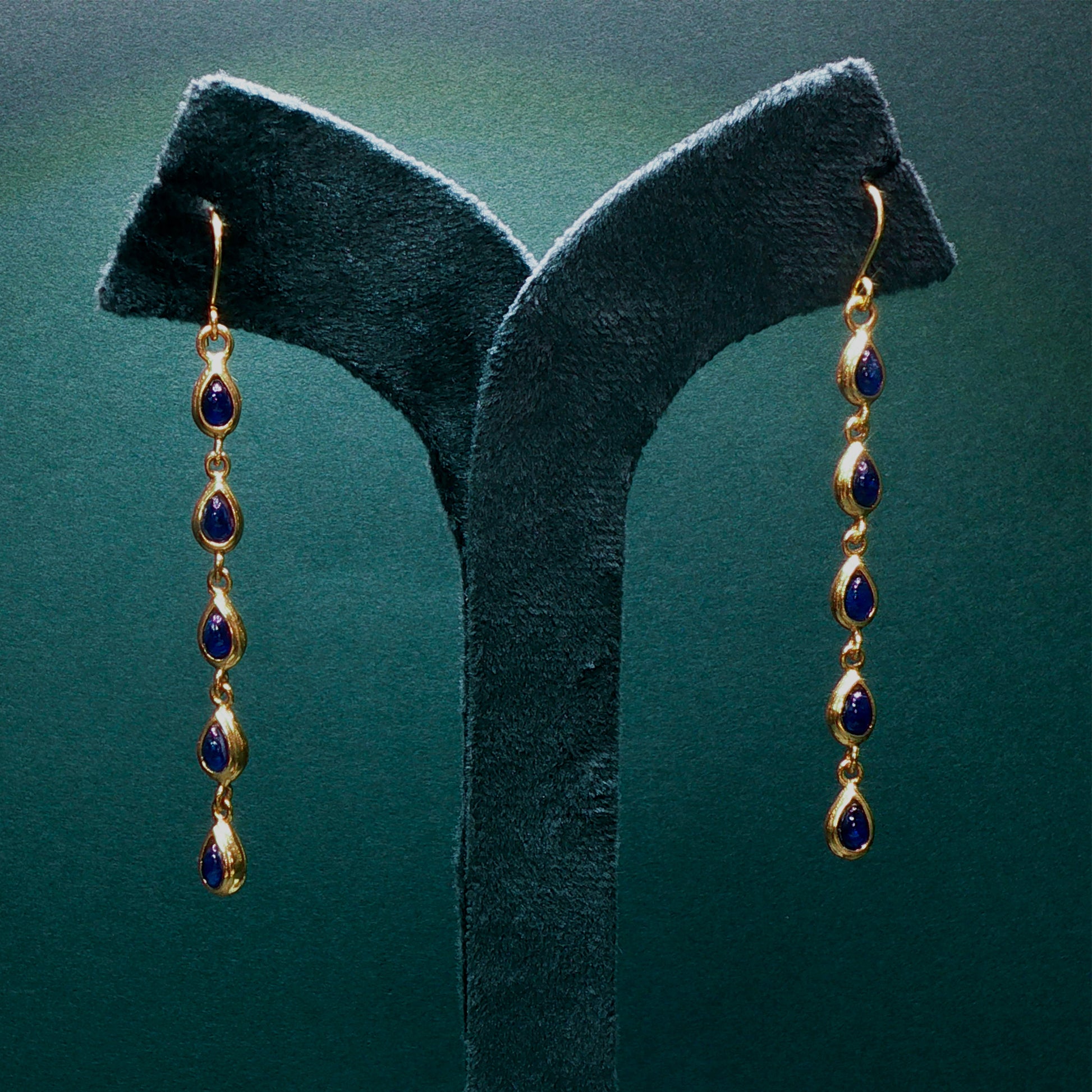 Gold earrings with blue stones on a green velvet stand