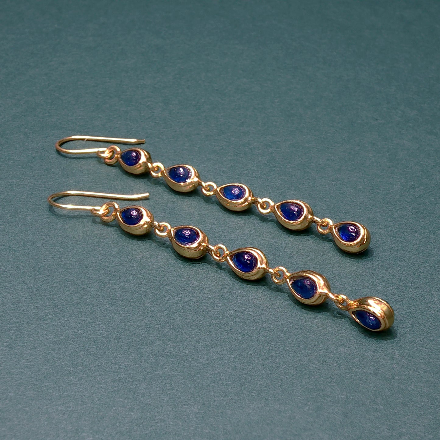 Gold earrings with blue gemstones on a teal background

