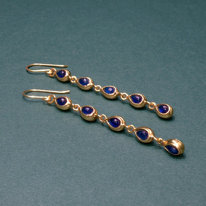Gold earrings with blue gemstones on a teal background

