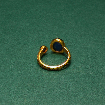 Gold ear cuff with a blue stone on a green background