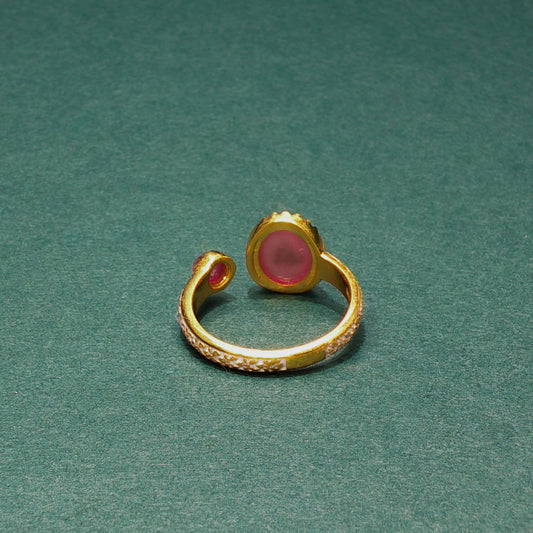 Gold ring with a pink gemstone on a green background