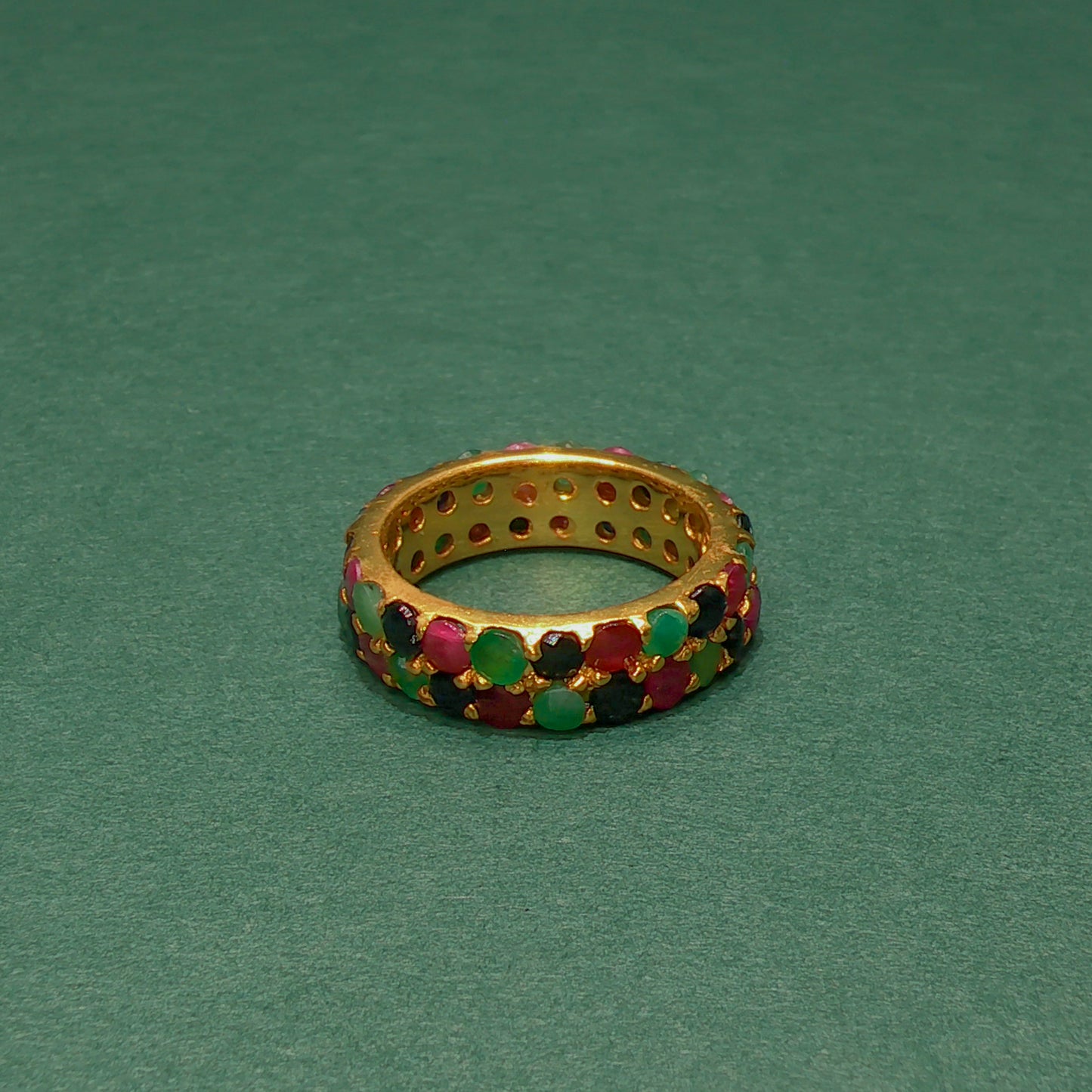 Gold ring with colorful gemstones on a green background