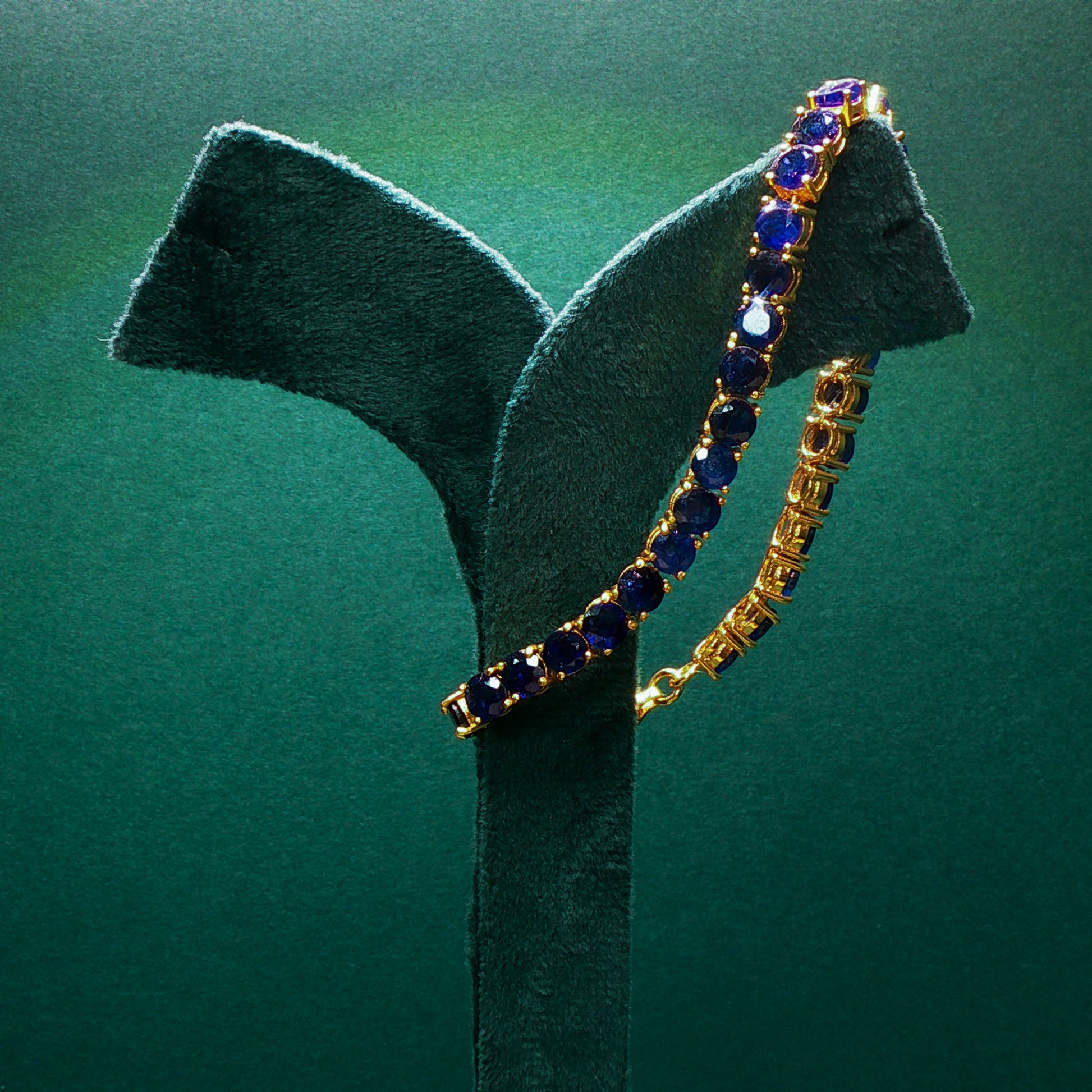 Gold bracelet with blue stones on a green stand against a green background