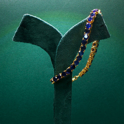 Gold bracelet with blue stones on a green stand against a green background