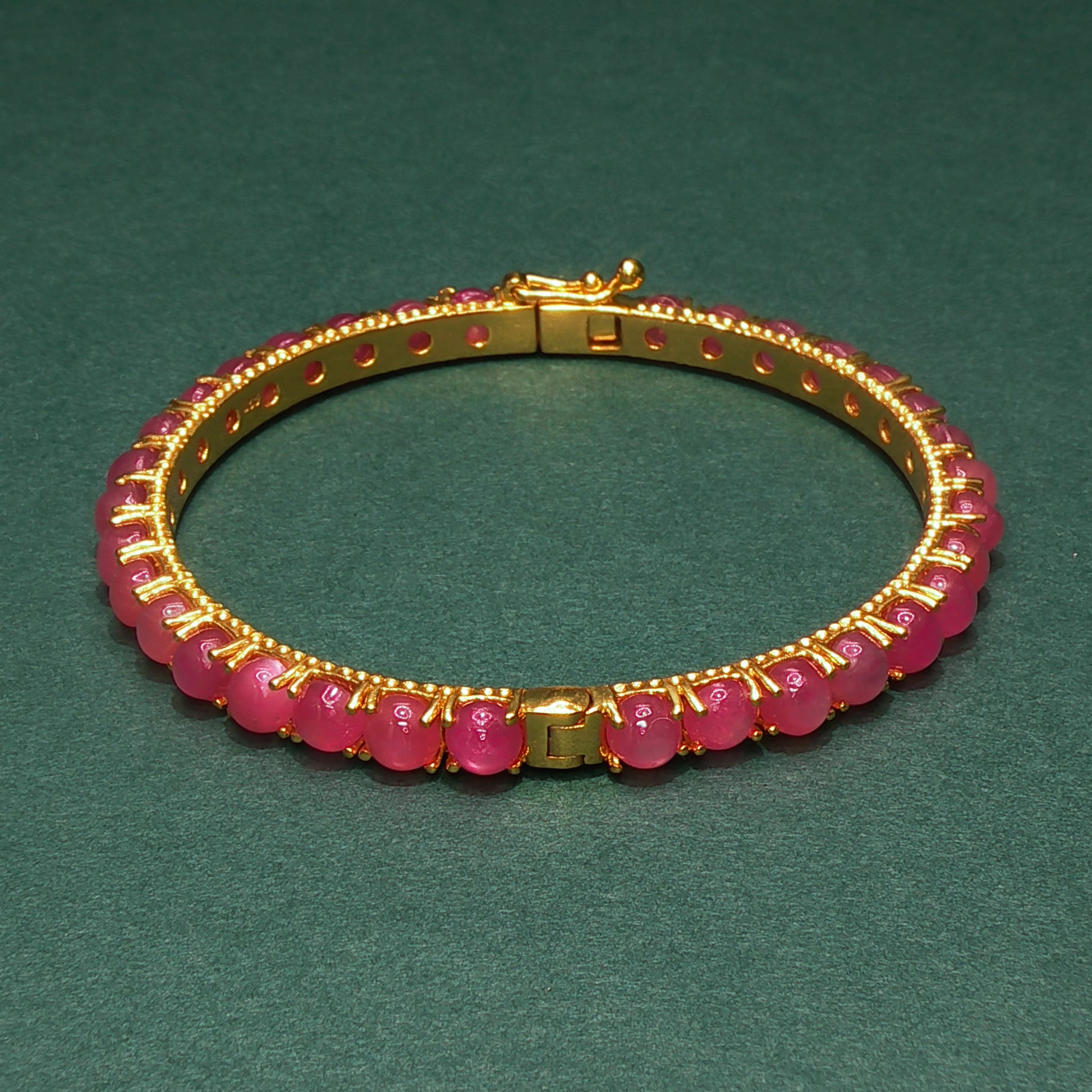 Gold bracelet with pink beads on a green background

