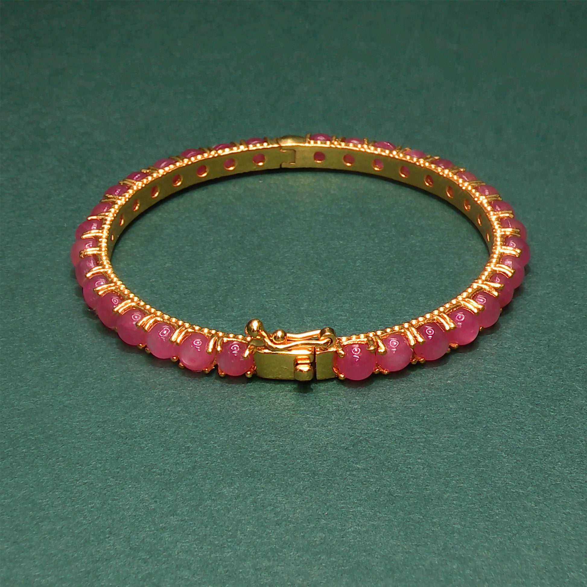 Gold bracelet with pink beads on a green background

