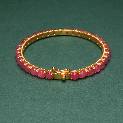 Gold bracelet with pink beads on a green background

