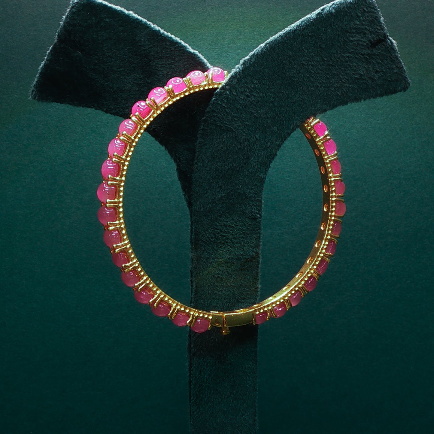 Gold hoop earring with pink beads on a green stand

