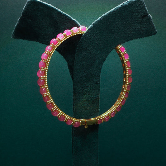 Gold hoop earring with pink beads on a green stand

