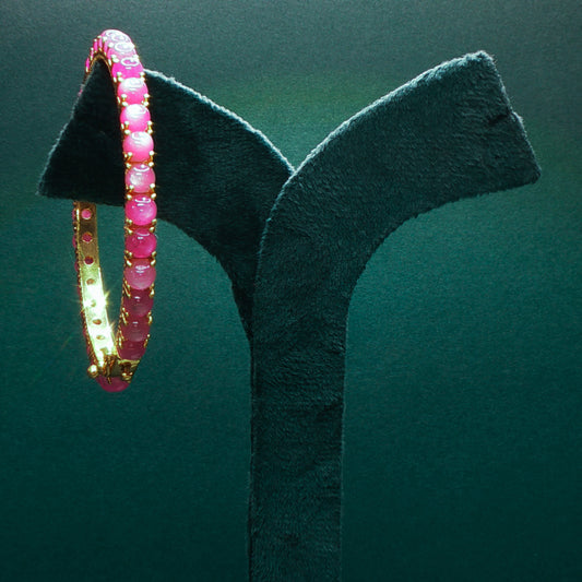 Pink beaded bracelet on a black stand against a green background

