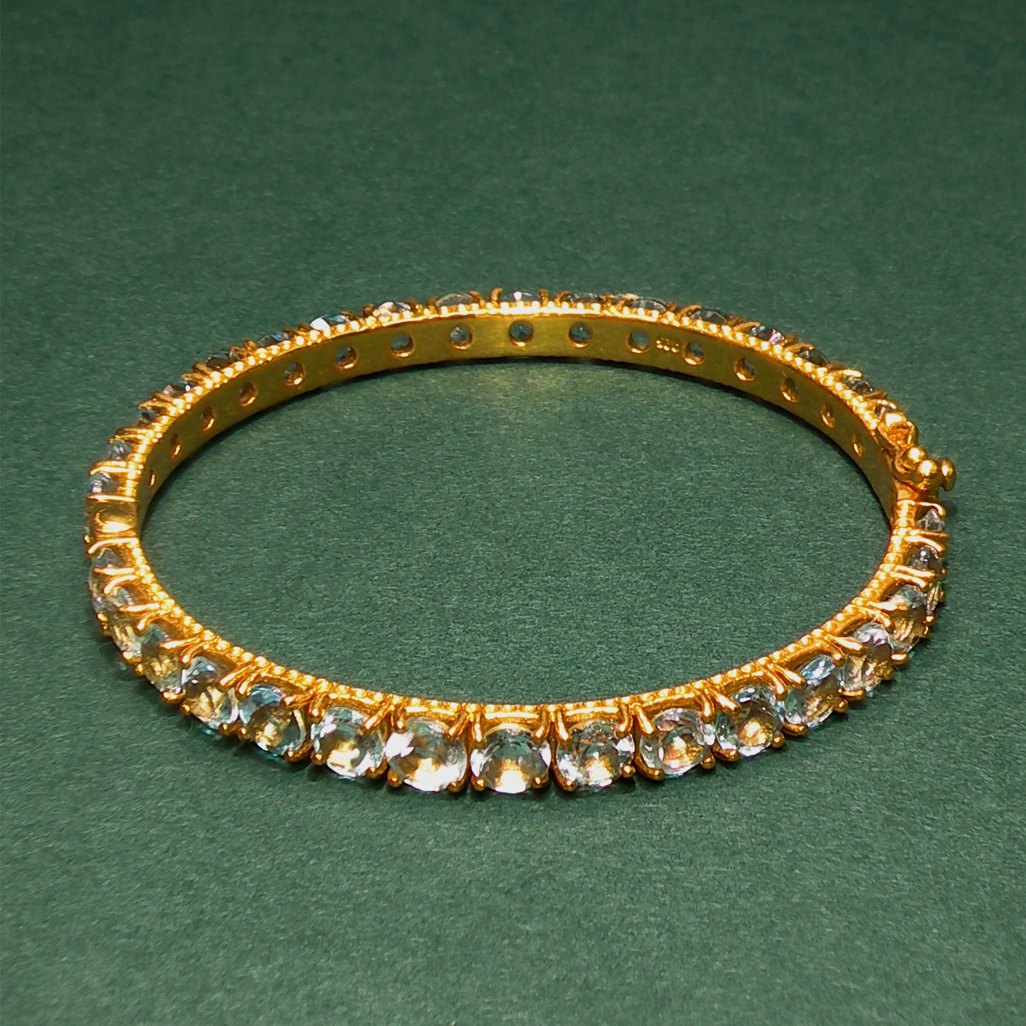 Gold bracelet with gemstones on a green background

