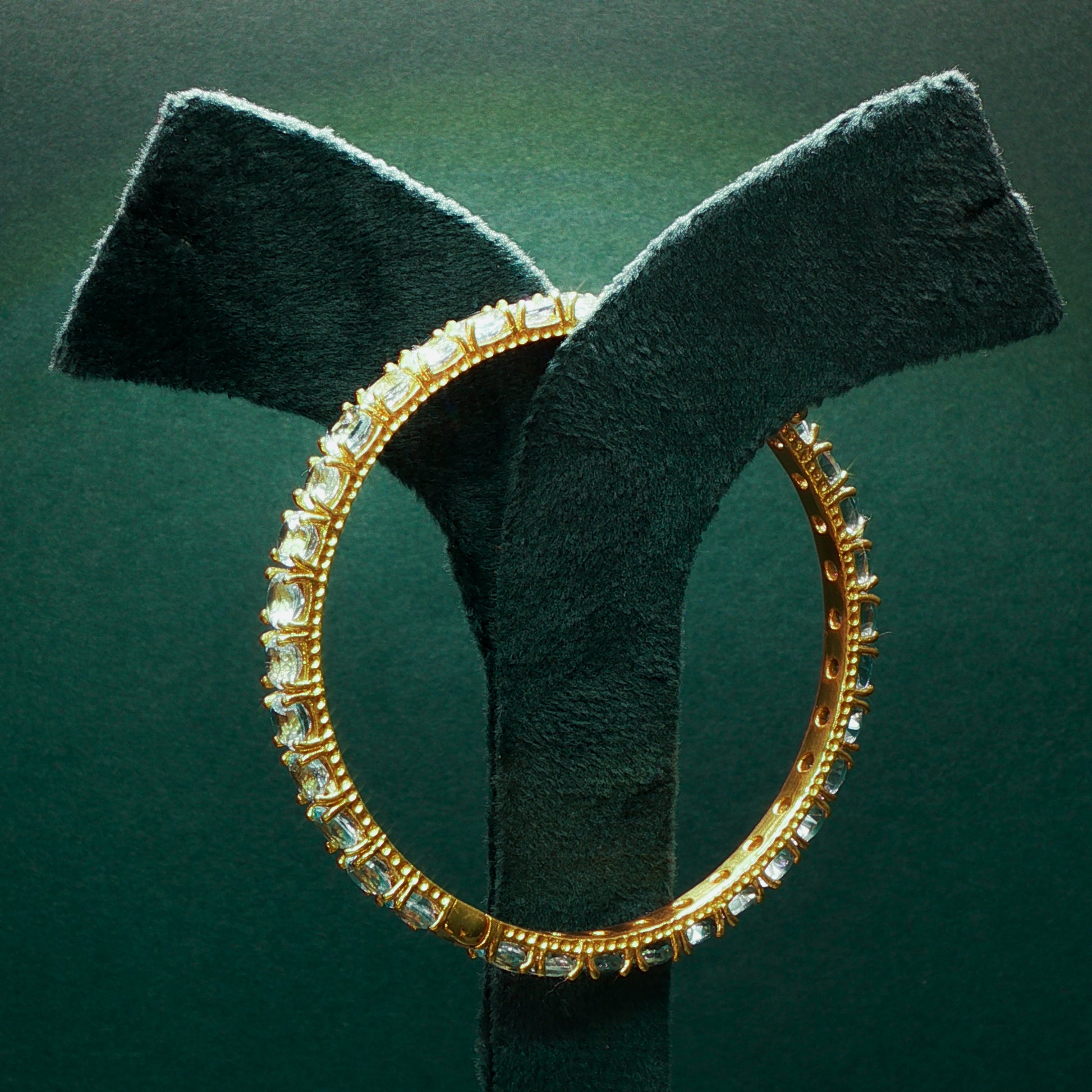 Gold hoop earring with clear stones on a green stand against a dark green background