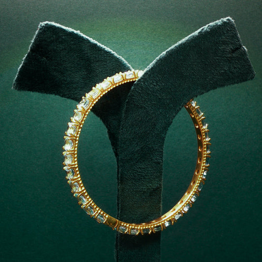 Gold hoop earring with clear stones on a green stand against a dark green background