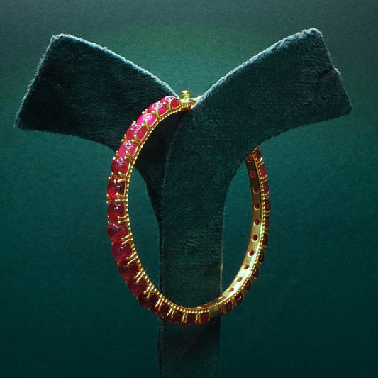 Gold hoop earring with red gemstones on a green stand