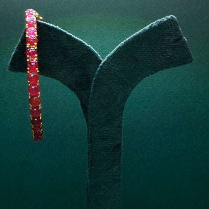 Gold bracelet with gemstones on a green stand

